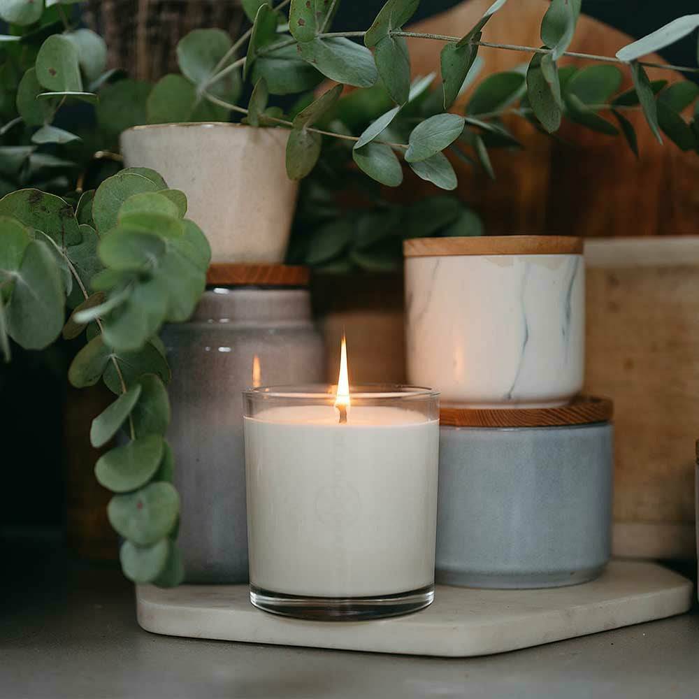 CandleXchange 400g glass candle sitting in front of canisters on bench with eucalyptus branches sitting behind