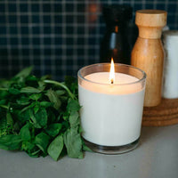 Lit CandleXchange candle on kitchen bench next to bunch of basil